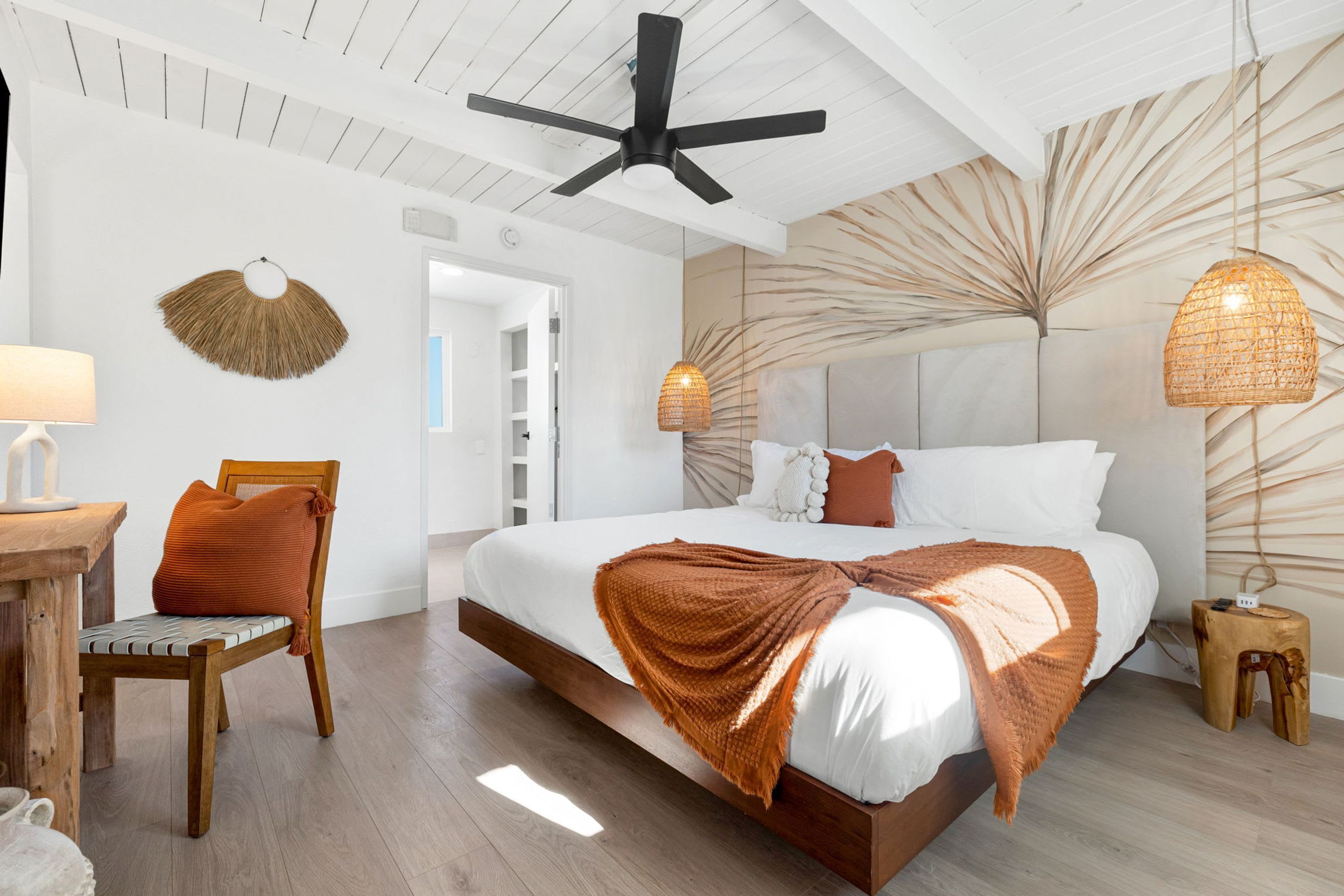 A modern bedroom with a large bed, a ceiling fan, and a wall-mounted lamp.