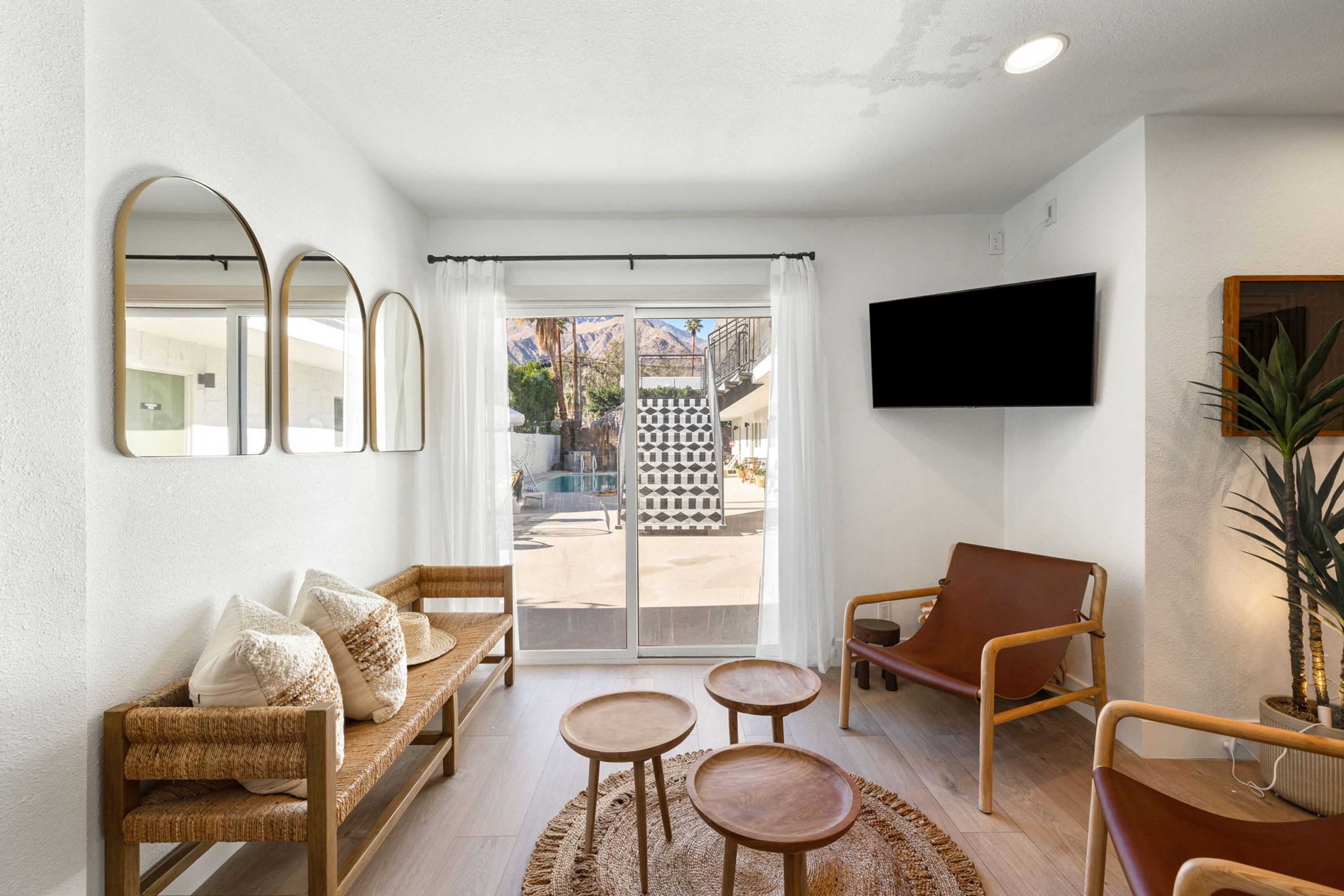 A modern living room with a sofa, two small tables, a brown leather chair, and a TV mounted on the wall.