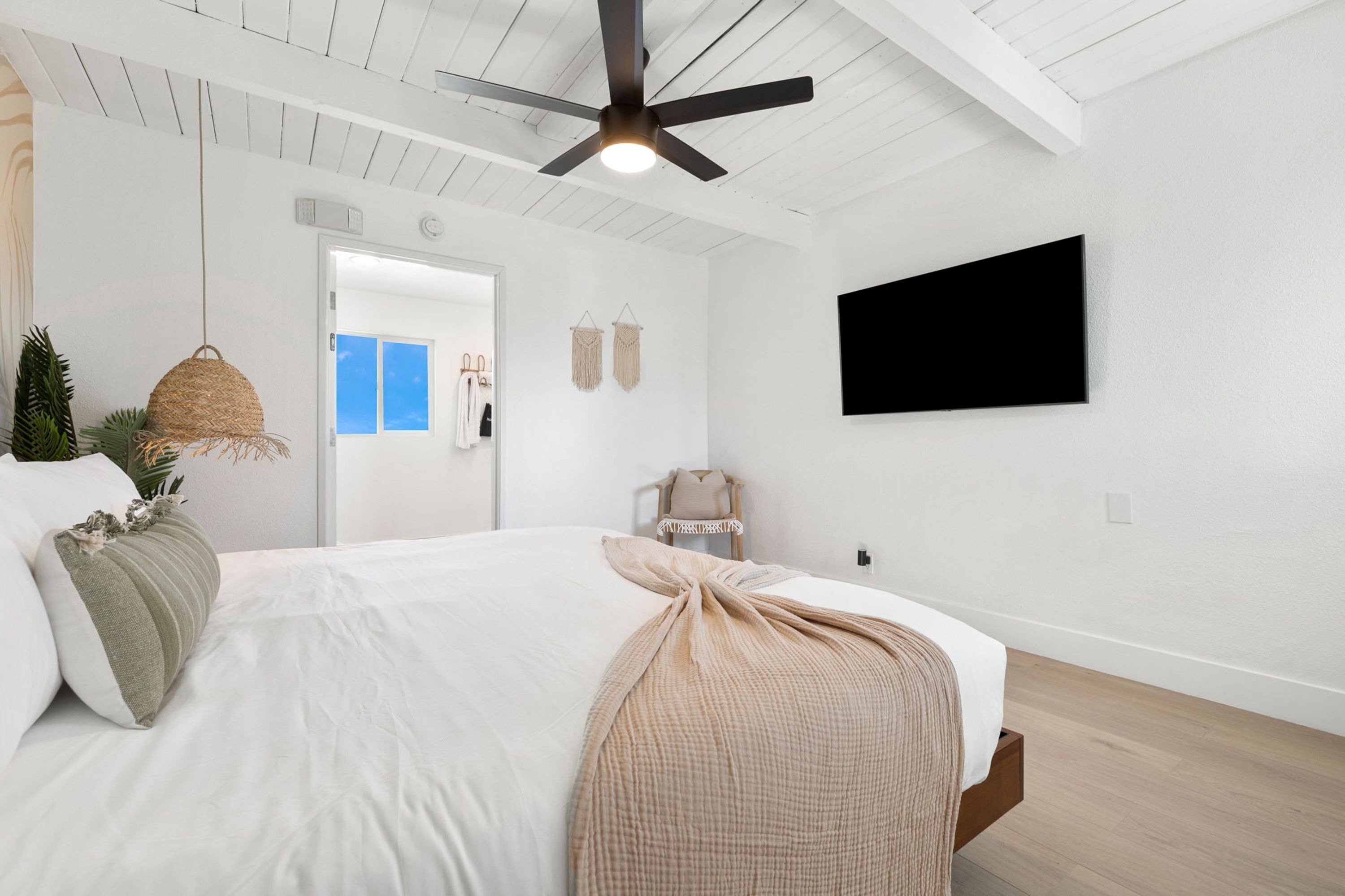 Ein modernes Schlafzimmer mit einem Bett, einem Deckenventilator, einem Fernseher und einer Tür zu einem weiteren Zimmer.