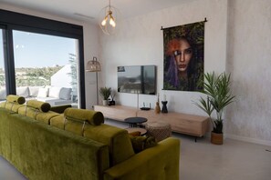 A modern living room with a green sofa, a flat-screen TV, a wooden bench, and a large window with a view of the landscape. - Casa la Vista by Bookaparadise (Finestrat)
