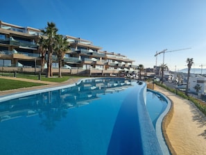 A modern hotel with a swimming pool, palm trees, and a view of the cityscape. - Casa la Vista by Bookaparadise (Finestrat)