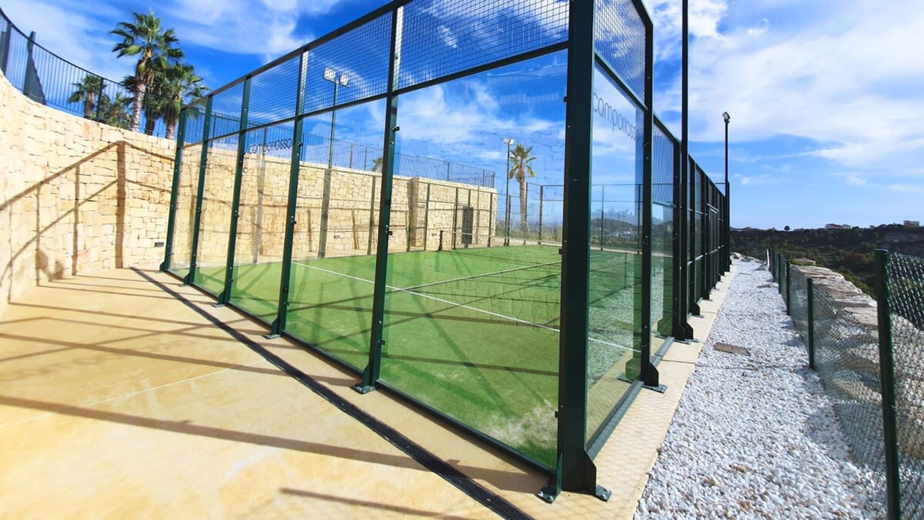 A tennis court with a net, surrounded by a stone wall and a metal fence.