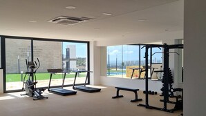 Un gimnasio amplio con cintas de correr, una banca y una estructura para sentadillas, con grandes ventanales que dan a una piscina y edificios.