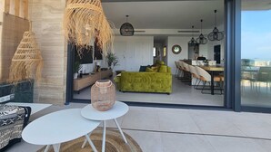 Un salon moderne comprenant un canapé, un coin repas avec des chaises et une grande porte-fenêtre coulissante donnant sur un espace extérieur.
