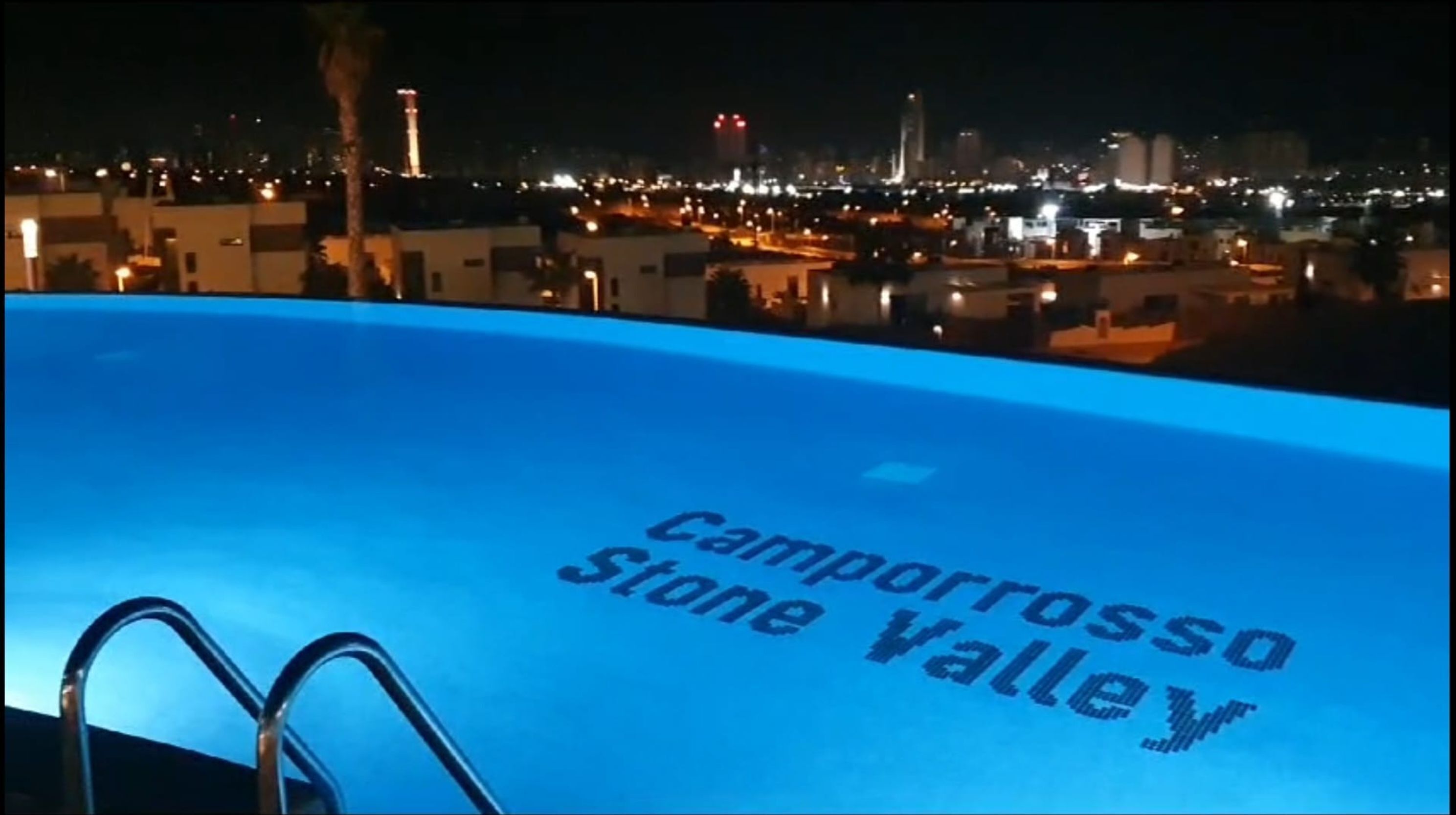 A swimming pool with "Camorrosso Stone Valley" text, surrounded by a cityscape at night.