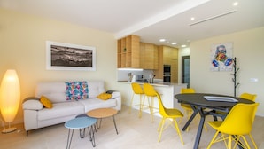 A modern living room with a white sofa, yellow chairs, a dining table, and a kitchen area with wooden cabinets. - Mediterranean Views by Bookaparadise (Finestrat)