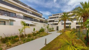 A modern apartment complex with multiple balconies, a central pathway, and lush landscaping including palm trees and flowering plants. - Mediterranean Views by Bookaparadise (Finestrat)