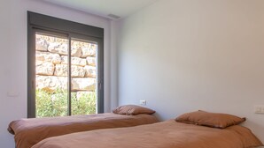 A bedroom with two beds, a stone wall visible through a window, and a tiled floor. - Villa Esmeralda 20 by Bookaparadise (Finestrat)