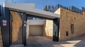 A modern building entrance with a stone facade, a covered walkway, and a garage door. - Villa Esmeralda 20 by Bookaparadise (Finestrat)