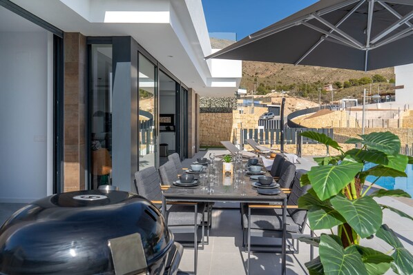 Un área de comedor al aire libre con una parrilla, mesa, sillas y una sombrilla grande.