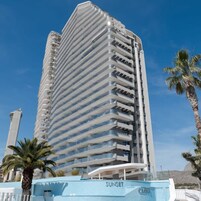 Un hotel alto y moderno con fachada curva, varios balcones y un cielo azul despejado al fondo.
