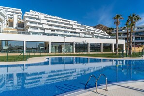 Un hôtel moderne doté d’une piscine, de palmiers et offrant une vue sur une montagne en arrière-plan.