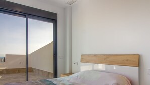 Une chambre à coucher avec un lit, une table de chevet, une tête de lit en bois, une porte-fenêtre coulissante et une vue sur le ciel.