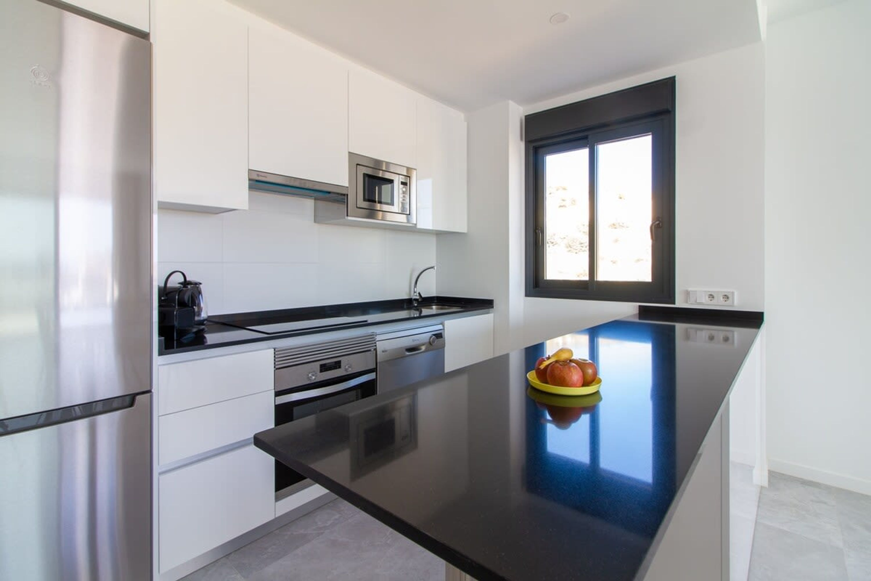A modern kitchen with white cabinets, a black countertop, a stainless steel refrigerator, and a microwave.