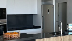 A modern kitchen with white cabinets, a black countertop, a stainless steel refrigerator, and a wooden accent wall. - Polop Hills 21A by Bookaparadise (Polop)