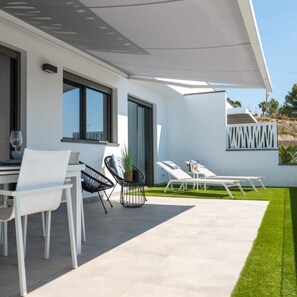 Een modern buitenterras met een eethoek, lounge stoelen en een kleine tafel.