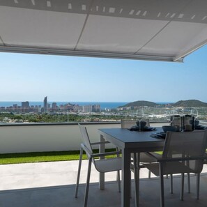 A rooftop terrace with a table set for dining, overlooking a city skyline and the sea.