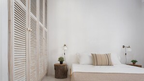 A bedroom with a bed, two bedside tables with lamps, a small plant, and a wooden stool. - Lea Villa 2 Mykonos (Mykonos Island)