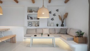 A modern living room with a white sofa, a wooden bench, a white coffee table, and a hanging light fixture. - Lea Villa 2 Mykonos (Mykonos Island)