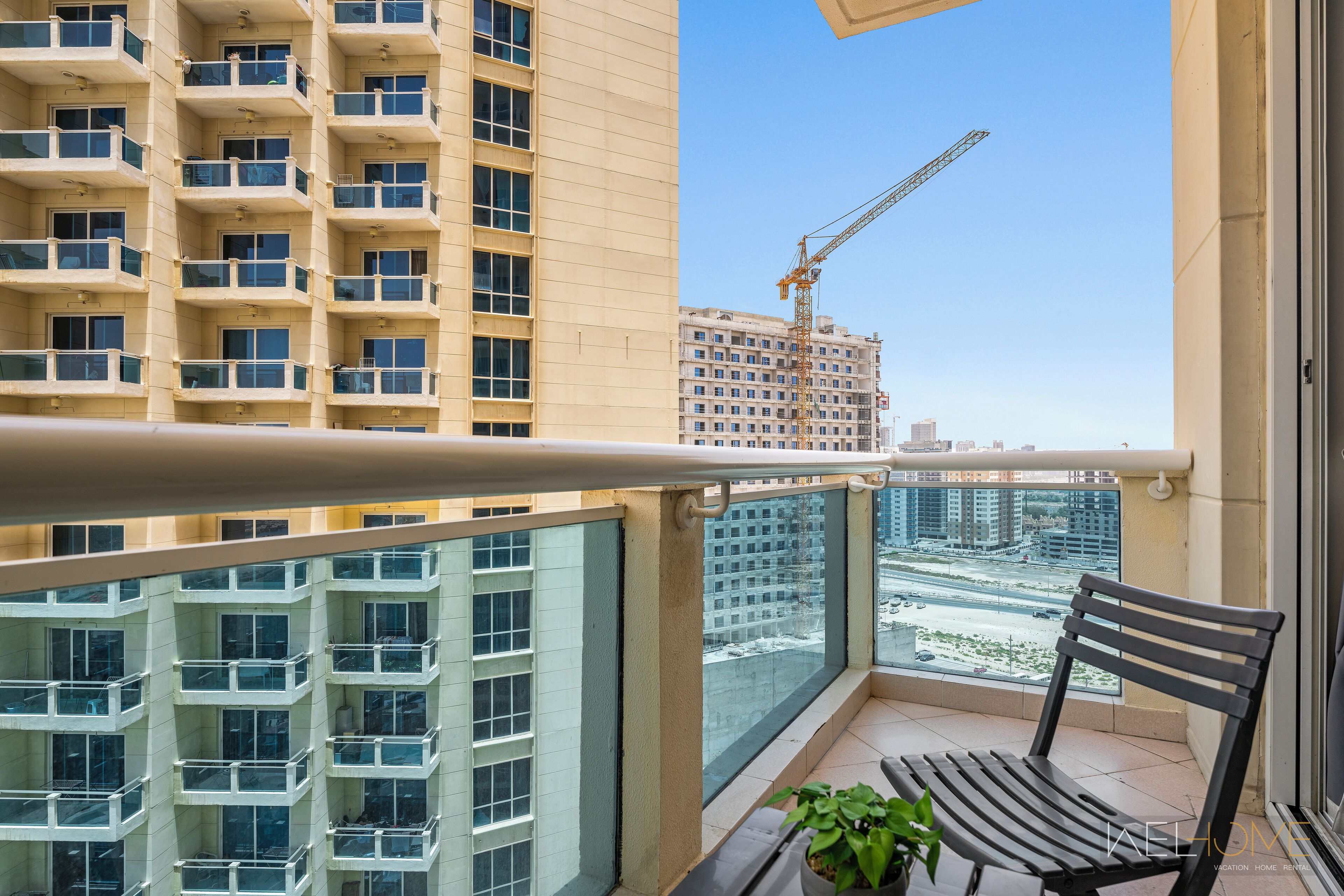 Un balcon donnant sur un chantier de construction avec une grue, un pot de fleurs et un banc en bois.