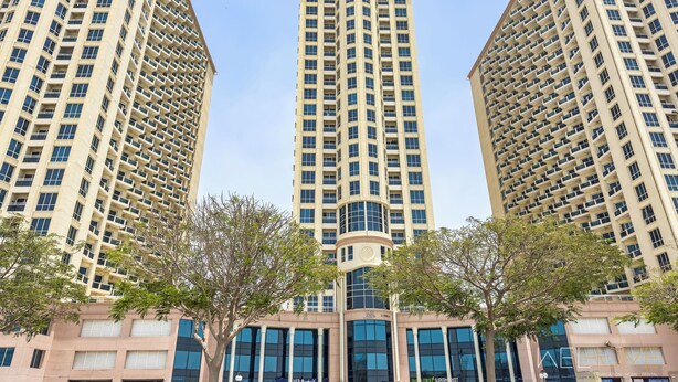 Three high-rise buildings with a central structure featuring a curved top. - WelHome - Greenery Apt for Modern Studio in Production City (Dubai)