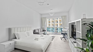 A modern bedroom with a large bed, a TV, a desk, and a balcony view. - WelHome - Greenery Apt for Modern Studio in Production City (Dubai)