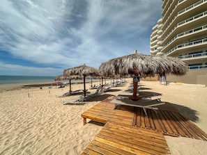A beach with sun loungers, thatched umbrellas, and a wooden deck. - Luxury Ocean View Condo w Huge Deck (Puerto Peñasco)