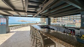 An outdoor bar area with a view of the beach and poolside lounge. - Luxury Ocean View Condo w Huge Deck (Puerto Peñasco)