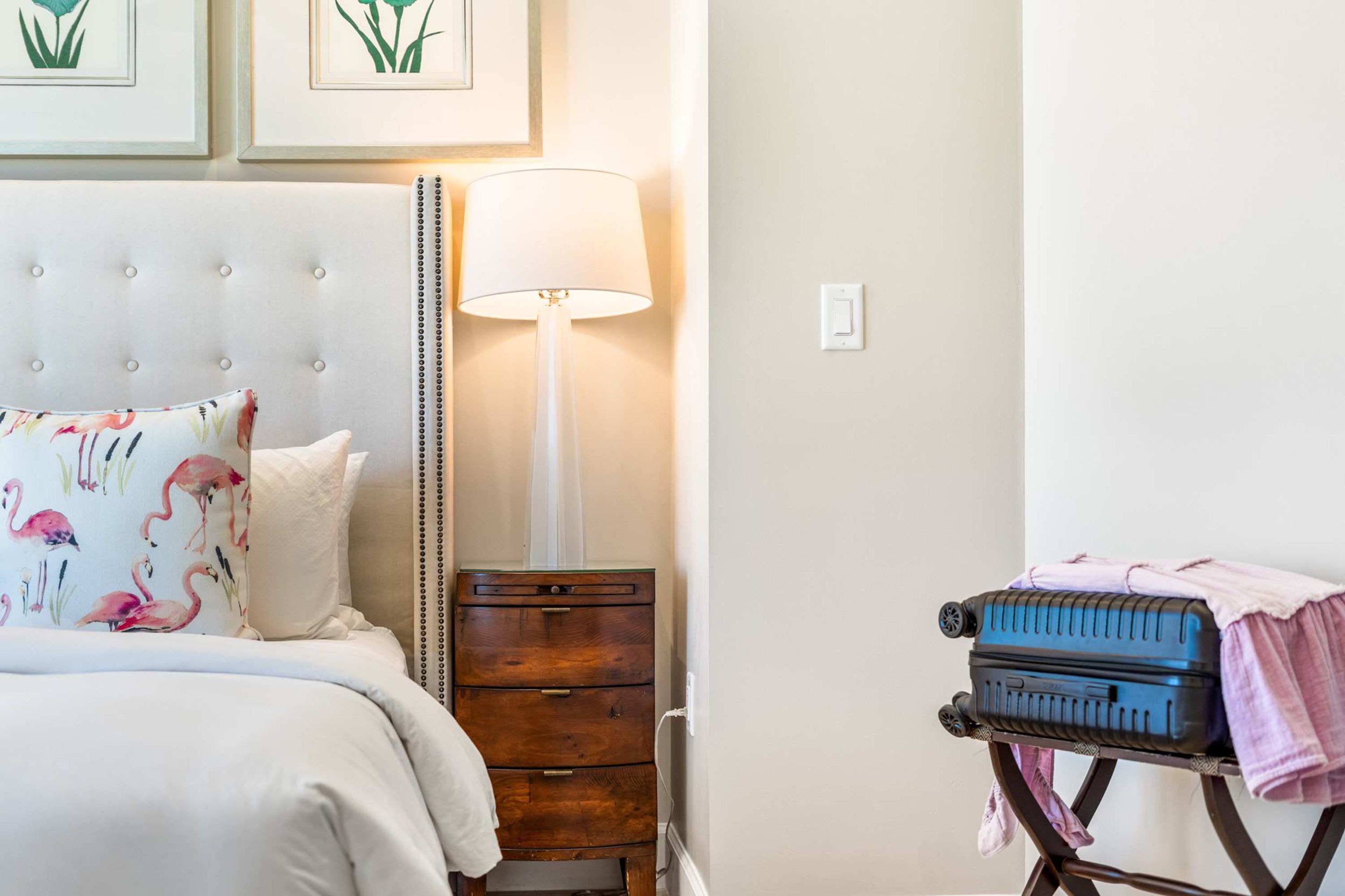 A bedroom with a bed, a bedside table, a lamp, a dresser, and a suitcase on a trolley.