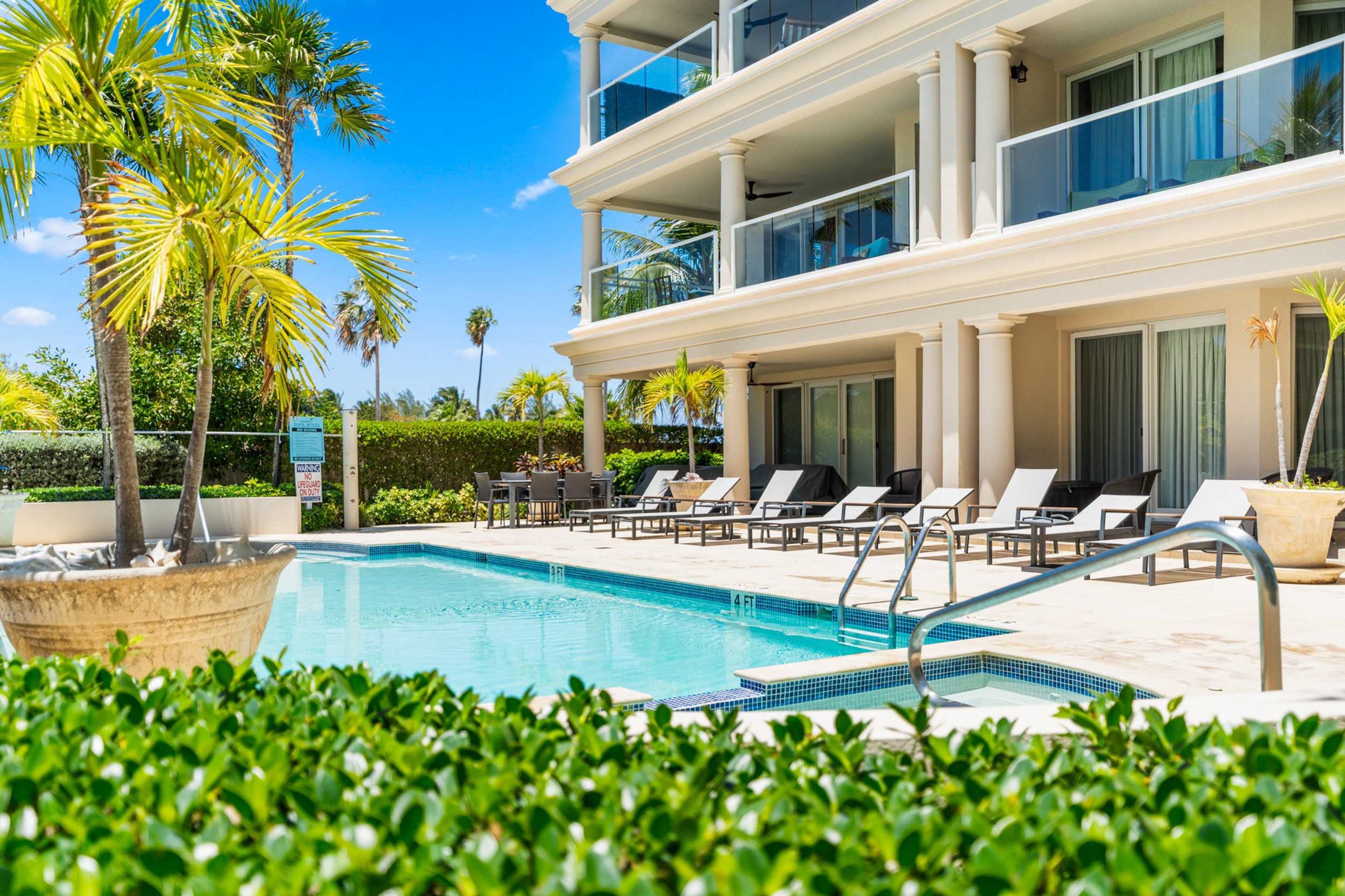 A pool area with lounge chairs, palm trees, and a building with balconies.