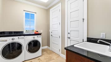 A laundry room with two front-loading washing machines, a window with a view, and a sink with a countertop.