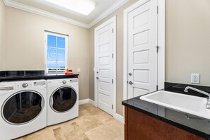 A laundry room with two front-loading washing machines, a window with a view, and a sink with a countertop. - Luxury Penthouse Condo With 360 Oceanviews (Seven Mile Beach)