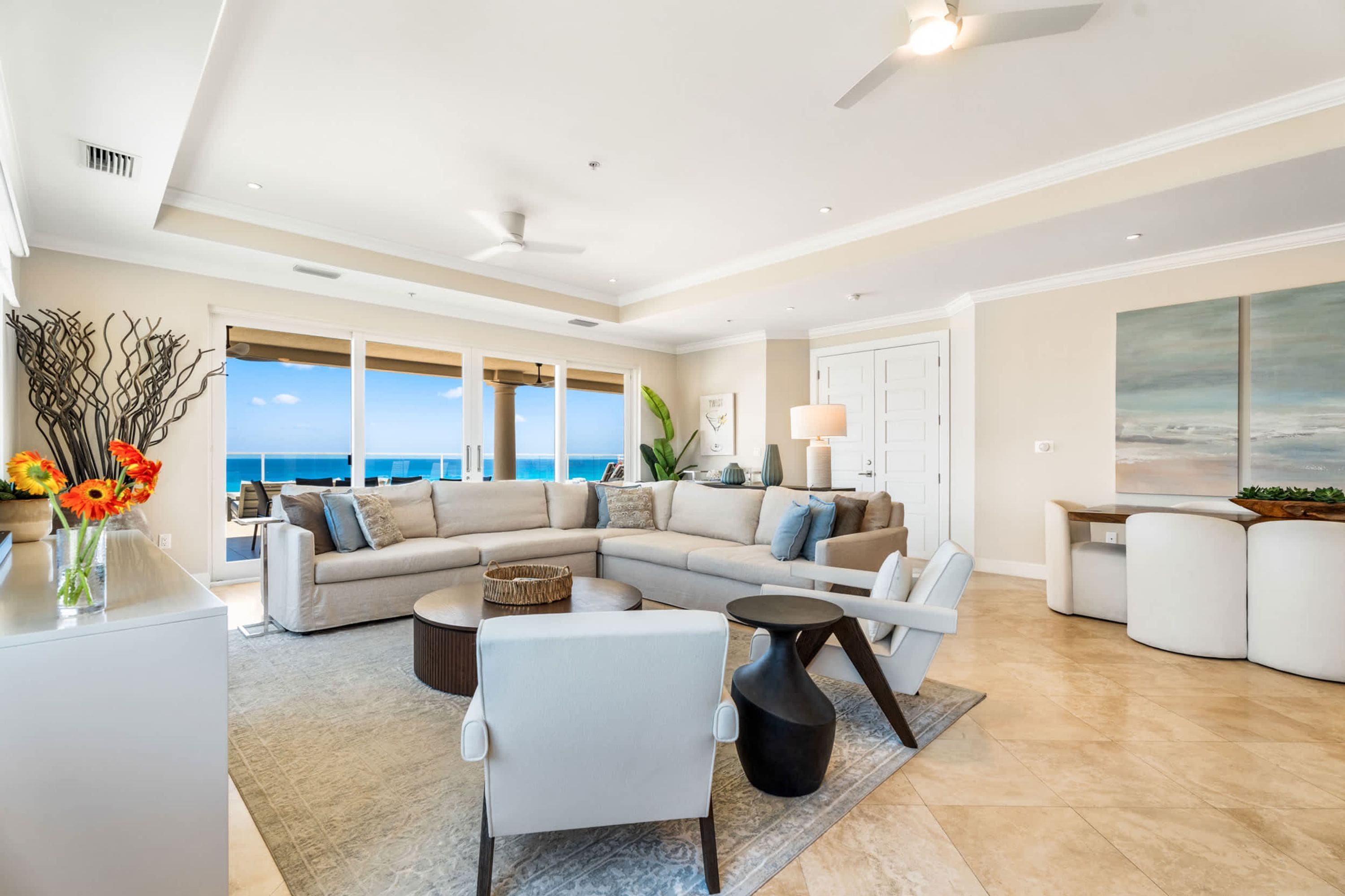 A spacious living room with a large window overlooking the ocean, a sectional sofa, a coffee table, and a modern fireplace.