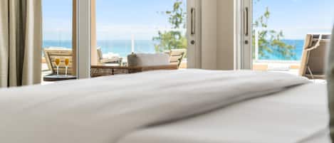 A hotel room with a bed, a view of the ocean, and a seating area with a table and chairs.