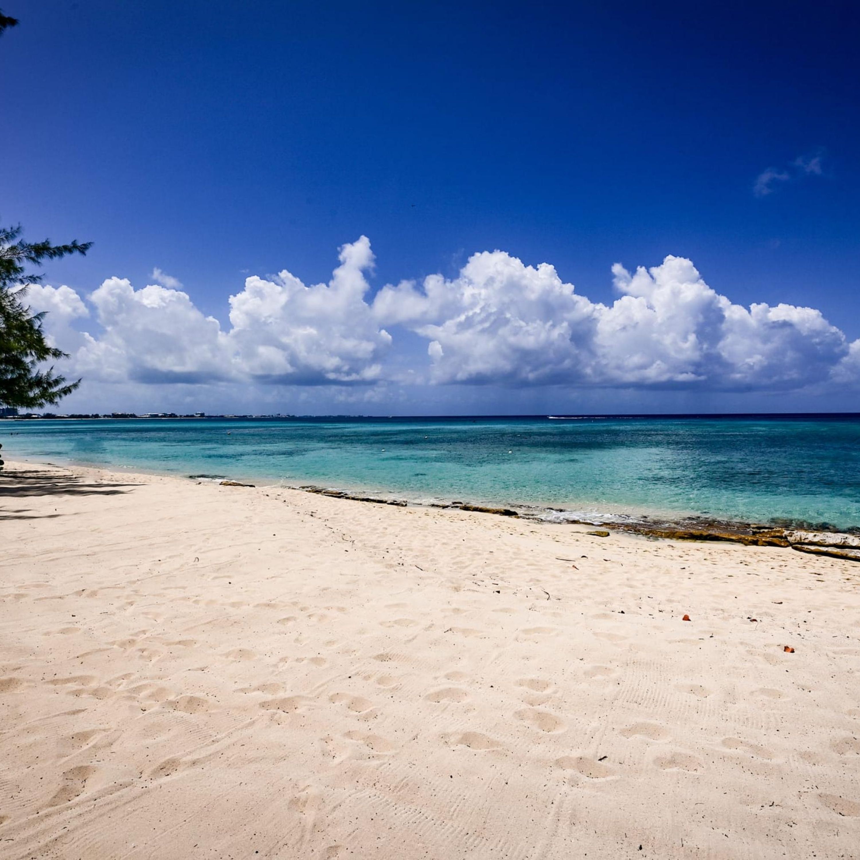 Ein Strand mit klarem türkisblauem Wasser, weißem Sand und vereinzelten Wolken am Himmel.