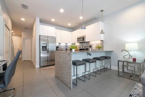 A modern kitchen with a central island, bar stools, stainless steel appliances, and pendant lighting. - Charming 3Bd w Pool Close to Disney Serenity 1639 (Clermont)