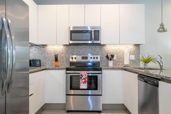 A modern kitchen with stainless steel appliances, granite countertops, and white cabinetry. - Charming 3Bd w Pool Close to Disney Serenity 1639 (Clermont)