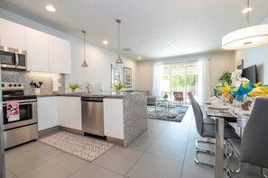 A modern kitchen with stainless steel appliances, a granite countertop, and a dining area with a table set for four. - Charming 3Bd w Pool Close to Disney Serenity 1639 (Clermont)