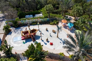 A water park with a pirate ship, palm trees, and a fenced area with seating.