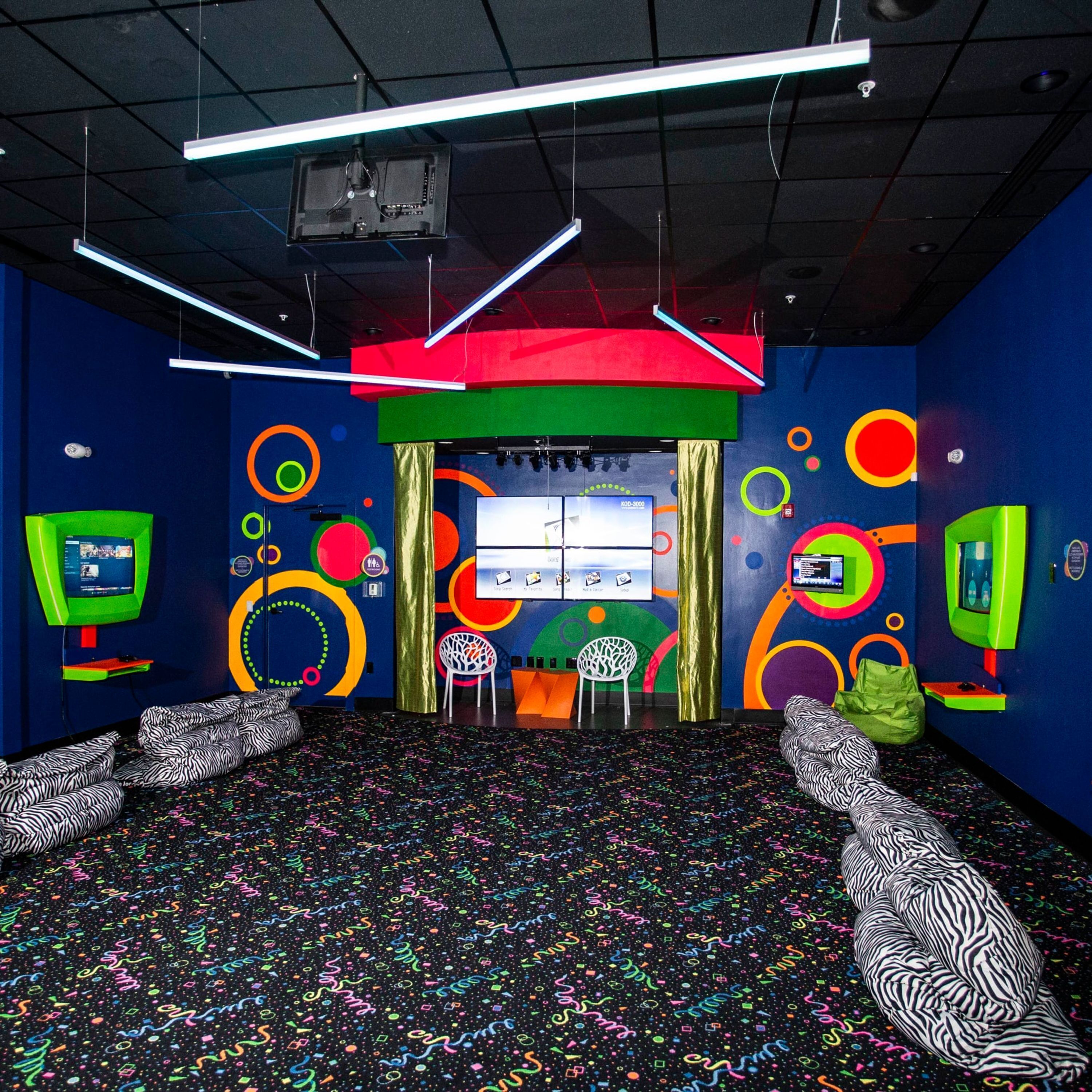 A room with a colorful abstract wall design, a large screen, and zebra-patterned seating.