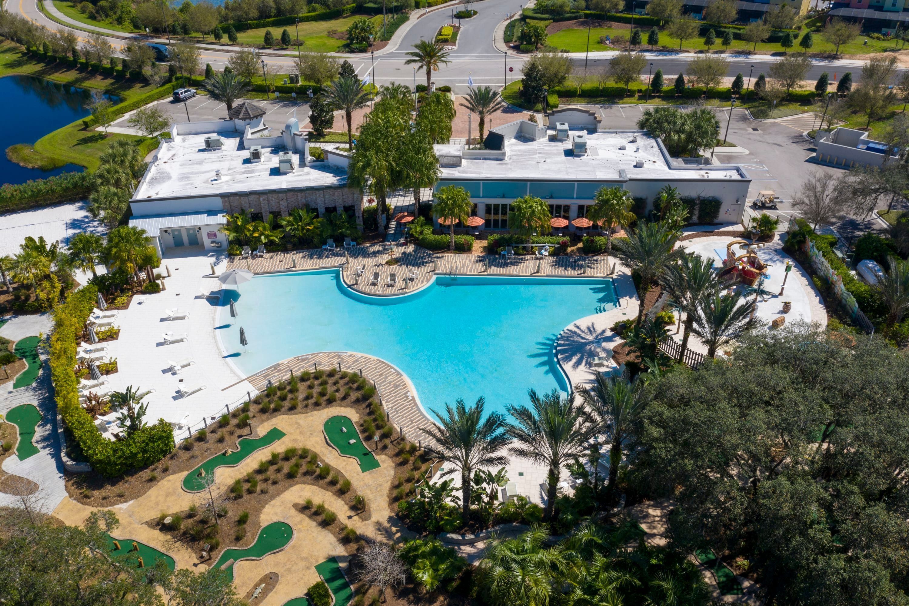 Vue aérienne d’un complexe hôtelier doté d’une grande piscine, d’espaces paysagers aménagés et d’un parking.