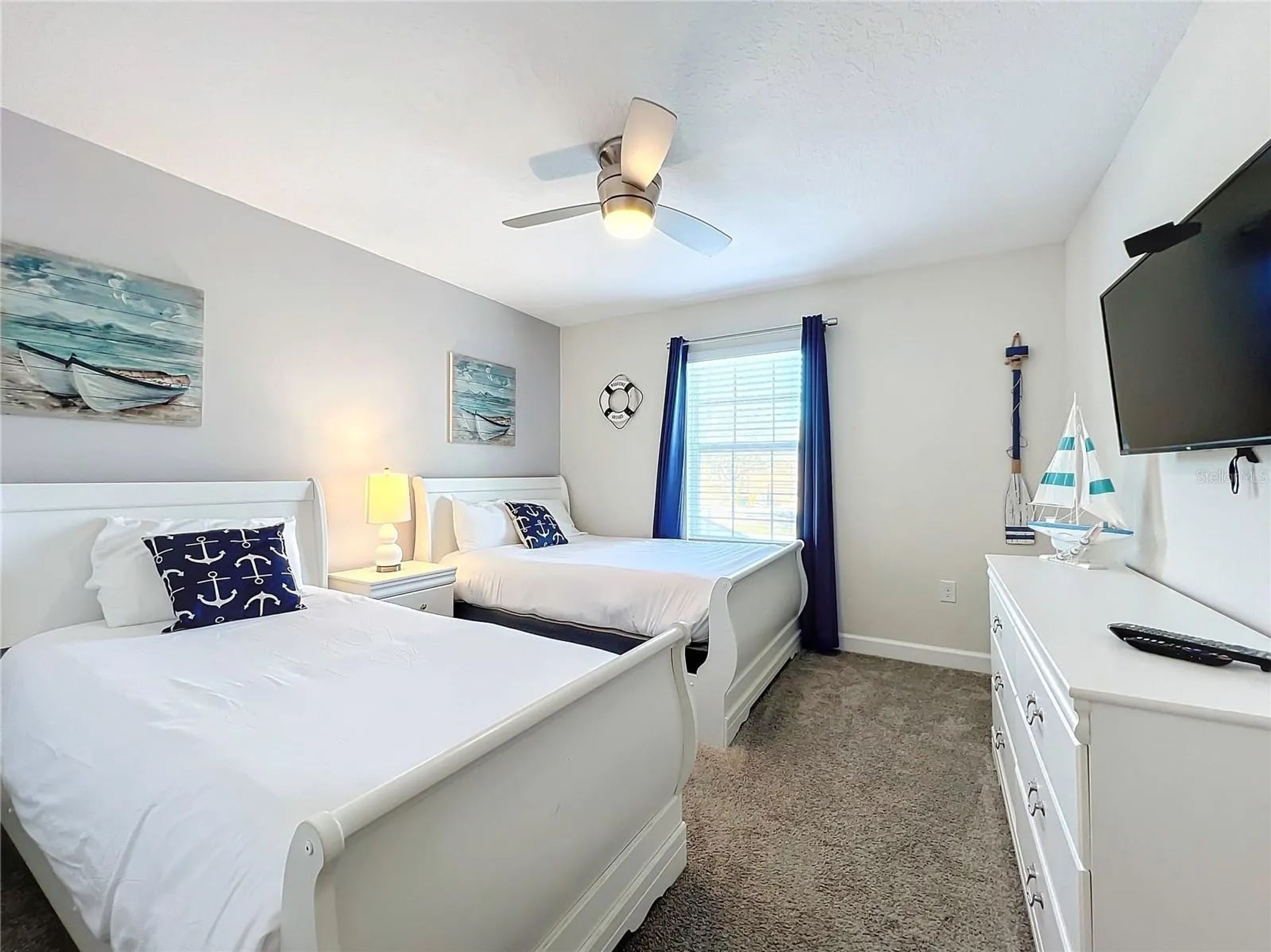 A bedroom with two beds, a ceiling fan, a TV, and nautical-themed decor.
