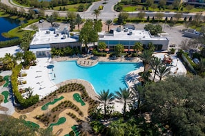 Luftaufnahme eines Resorts mit großem Schwimmbecken, angelegten Grünflächen und einem Parkplatz.