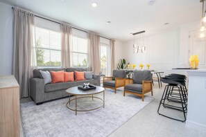 Ein modernes Wohnzimmer mit einem grauen Sofa, einem runden Couchtisch und einem Essbereich mit Holztisch und Stühlen.