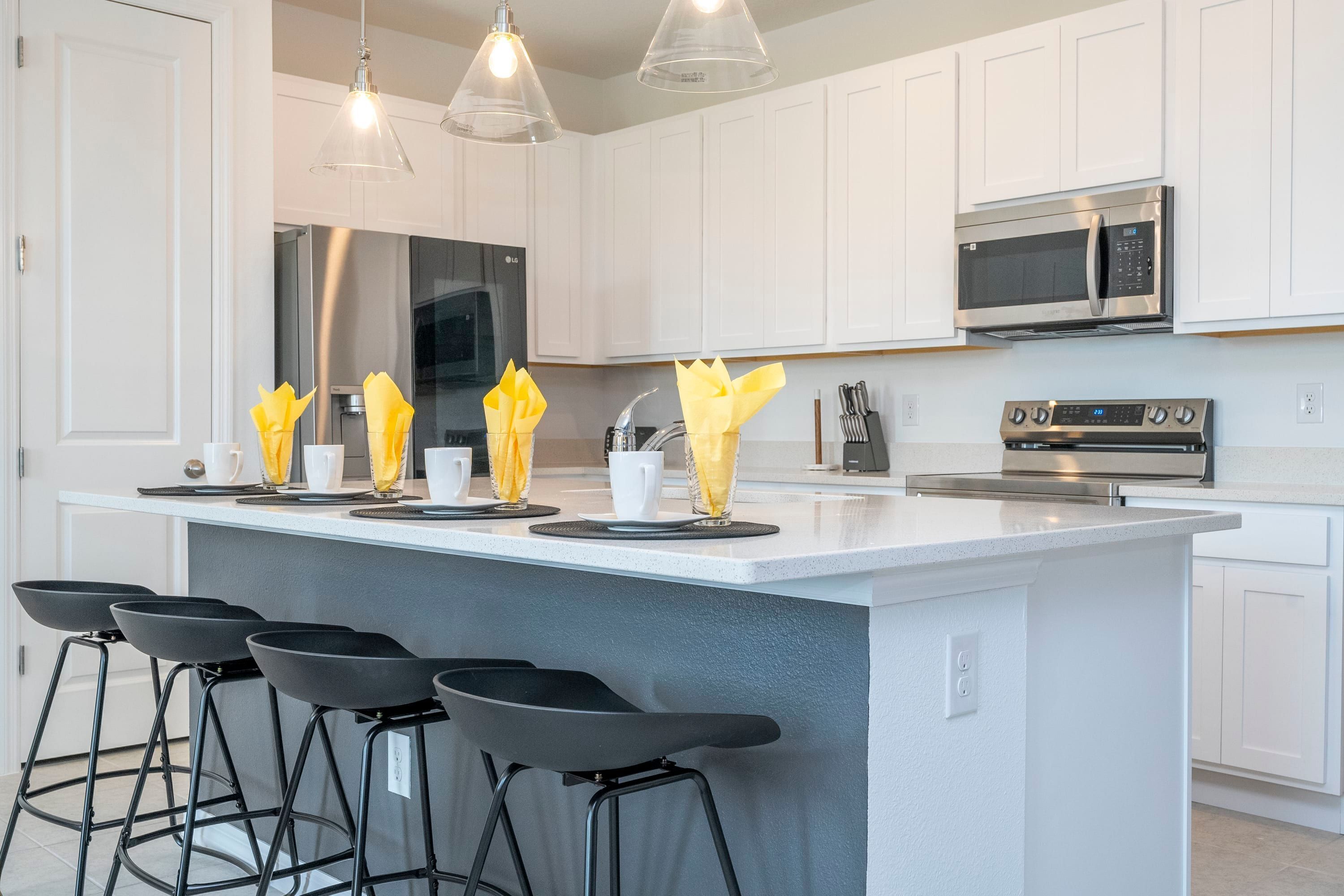 A modern kitchen with white cabinets, a large island with bar stools, stainless steel appliances, and pendant lighting.