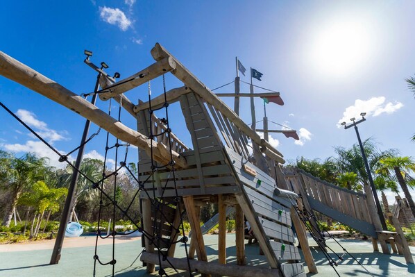 A wooden play structure with ropes and a slide, surrounded by greenery and palm trees. - 4Bd Close to Disney With Pool at Storey Lake 2560 (Kissimmee)