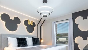 Ein modernes Schlafzimmer mit einem großen Bett, einer Mickey Mouse Wanddekoration und einem großen Fenster mit Vorhängen.