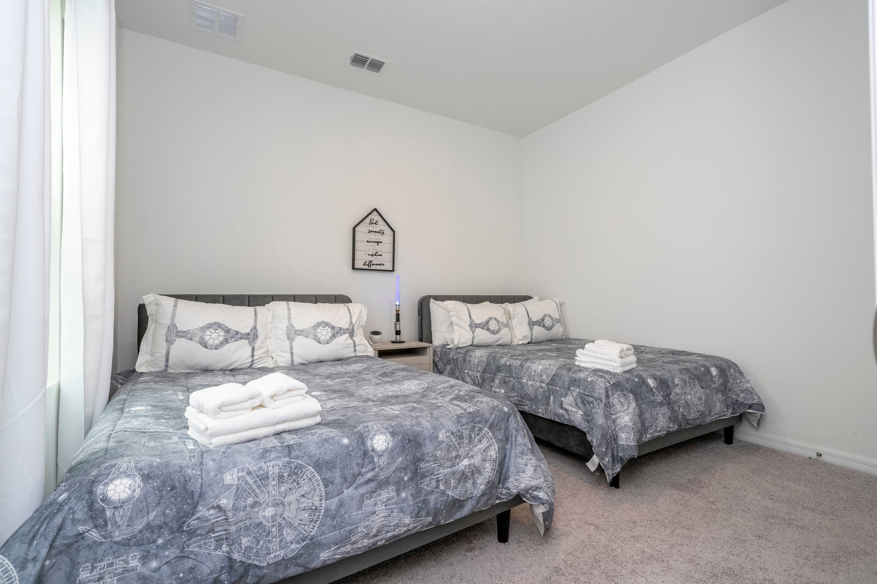 A bedroom with two beds, each with a galaxy-themed bedspread, white pillows, and a bedside table with a lamp.