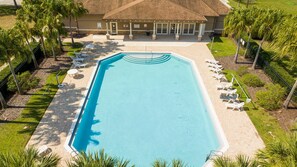 Ein rechteckiger Swimmingpool mit einer gefliesten Terrasse darum herum, eine überdachte Terrasse mit Stühlen und Palmen.