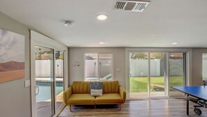 A spacious living room with a yellow sofa, a ping pong table, and a sliding glass door leading to a backyard. - Family Retreat By Old Town w Pool (Phoenix)